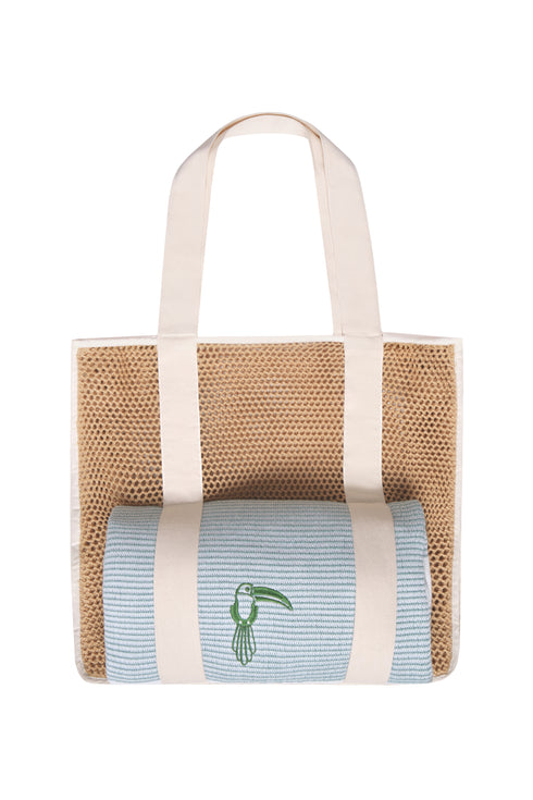 Mesh beach bag with cream straps holding a rolled light blue towel with a green toucan embroidery.