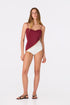Woman wearing a purple and ivory one-piece swimsuit with hand-embroidered shell detailing.