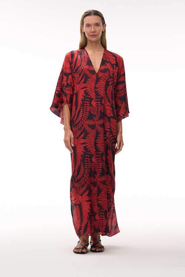 A woman wears a floor-length silk jacquard tunic in a red and black cherry rainforest print.